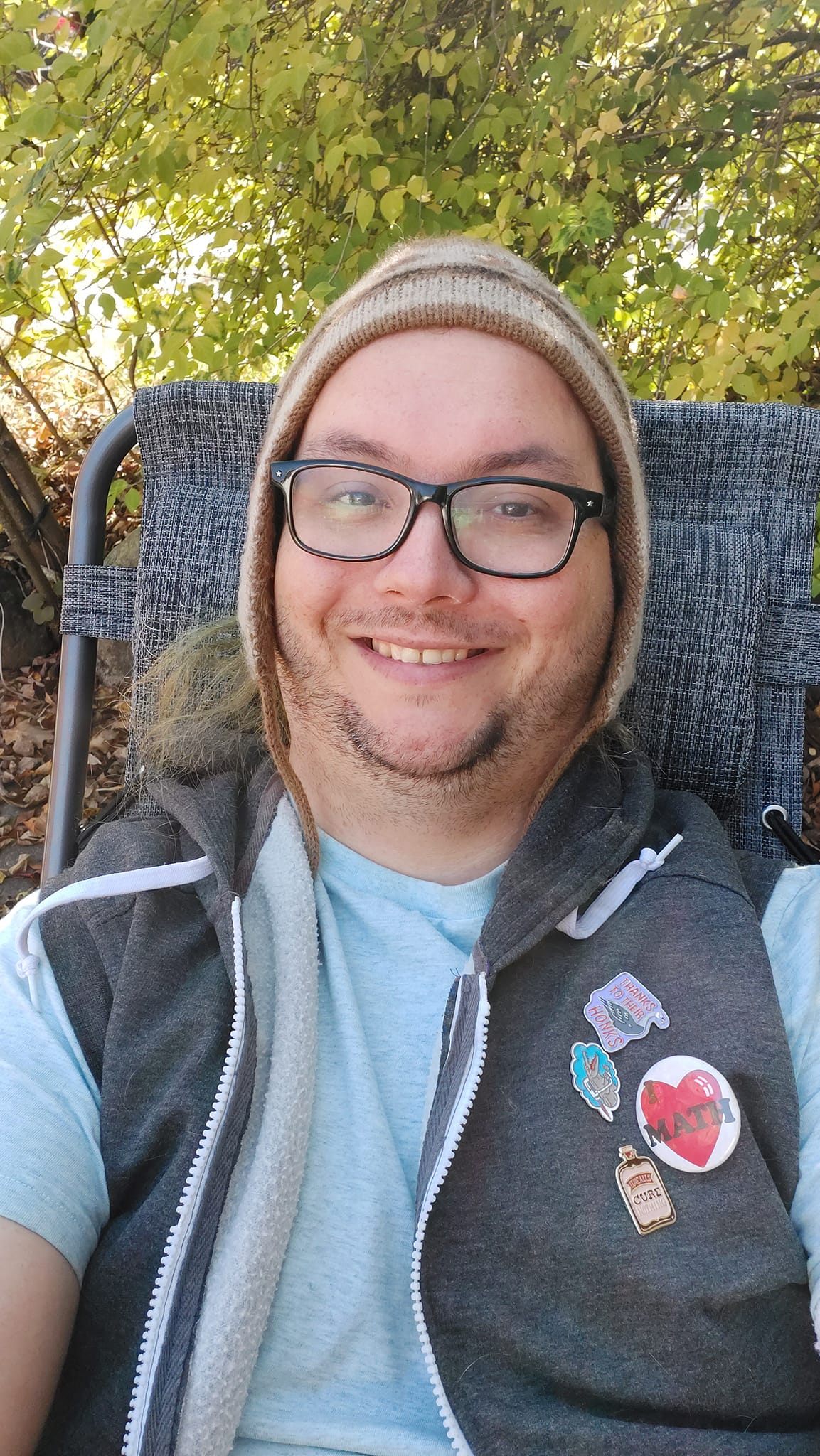 A man is wearing a toque with triangular flaps that cover the ears, sitting in a reclining lawn chair